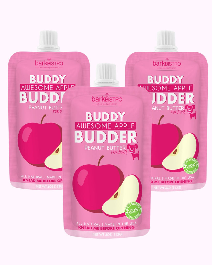 Three pink squeeze packs of Awesome Apple Buddy Budder natural dog peanut butter with apple graphics